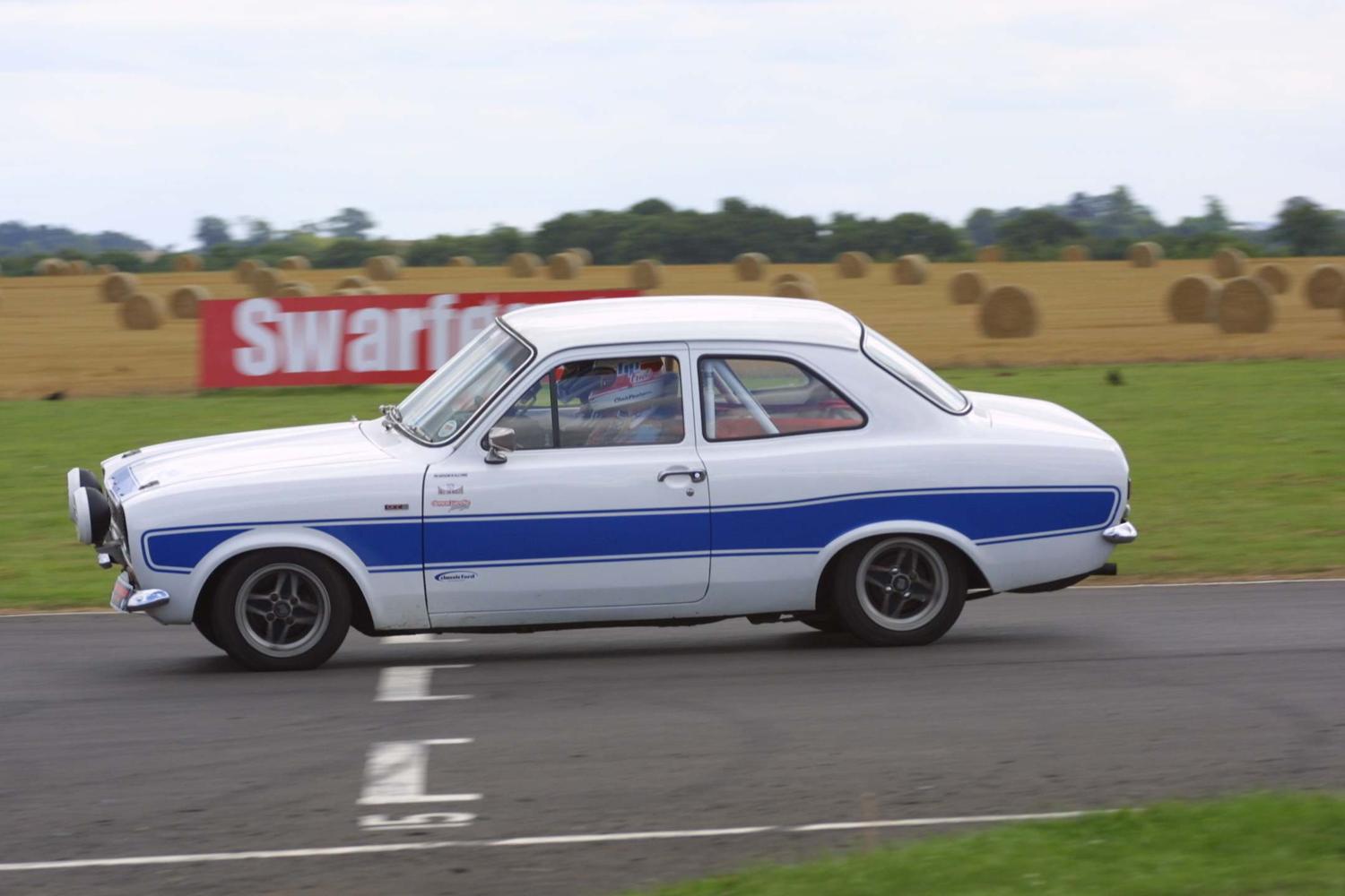 A white Mk1 Ford Escort with blue stripes on track